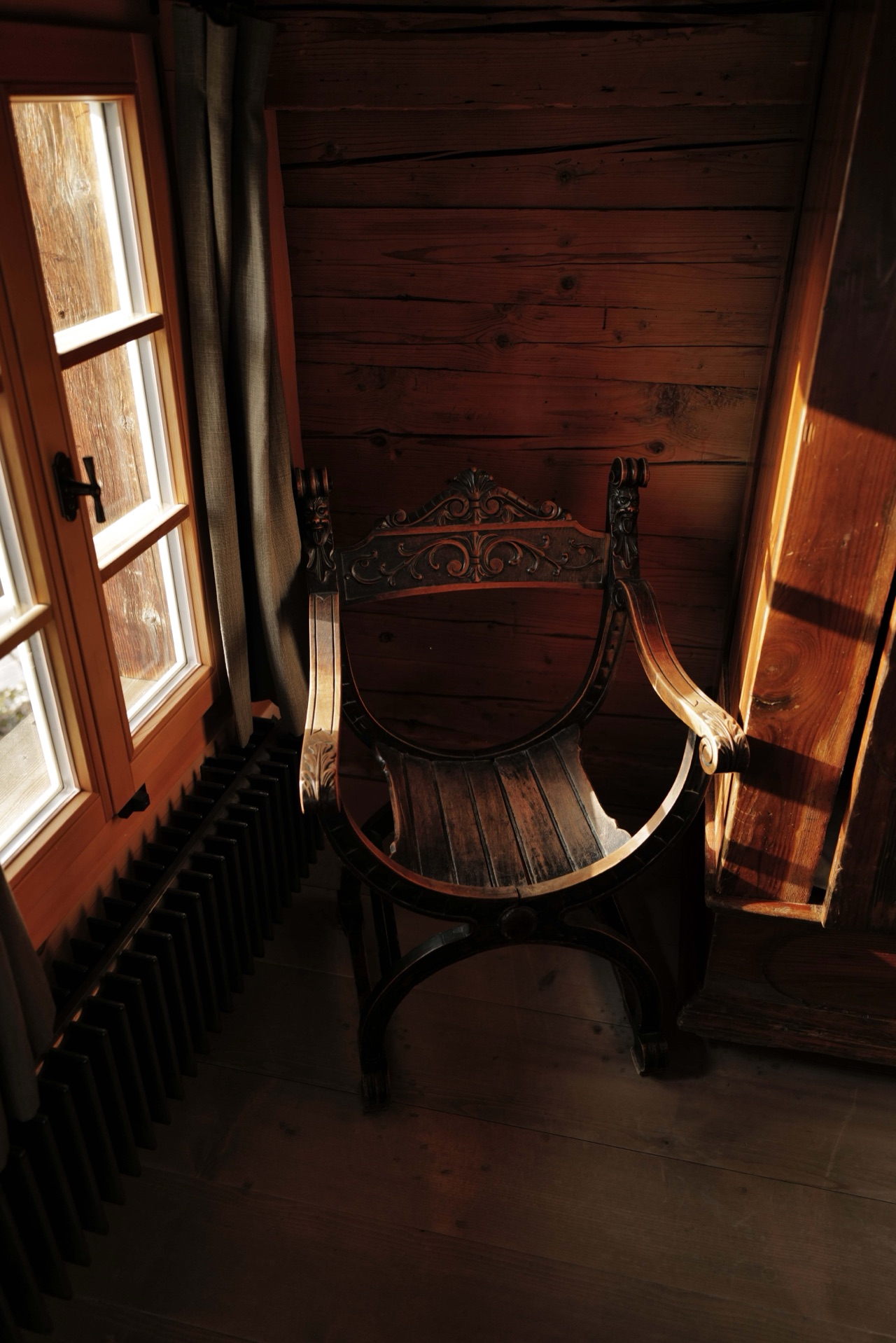 Ornate antique Savonarola chair by the window with dappled sunlight