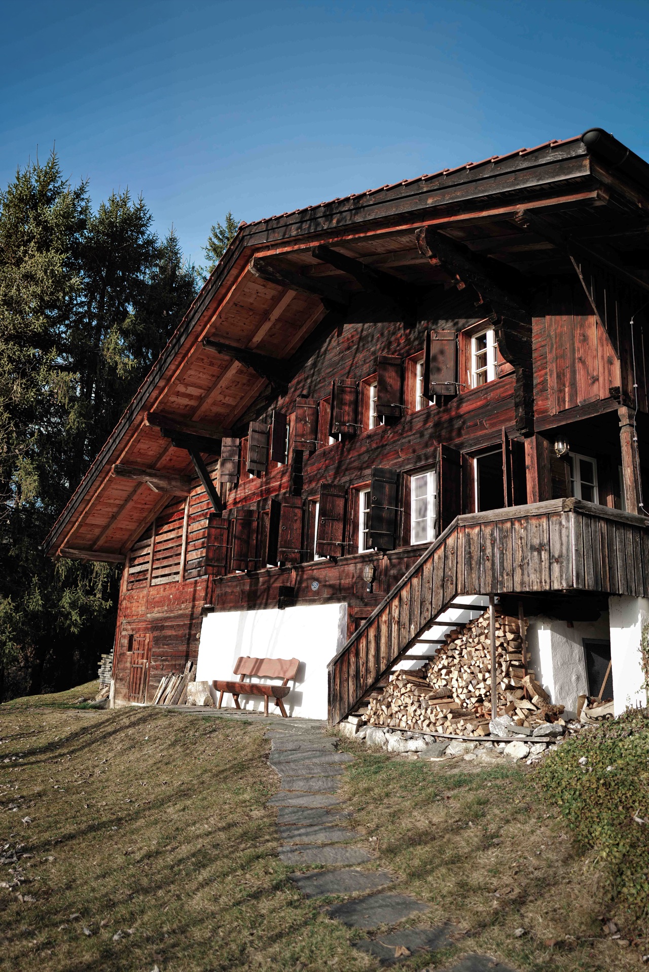 Full exterior of Chalet Amalia with stone path, firewood store and blue sky