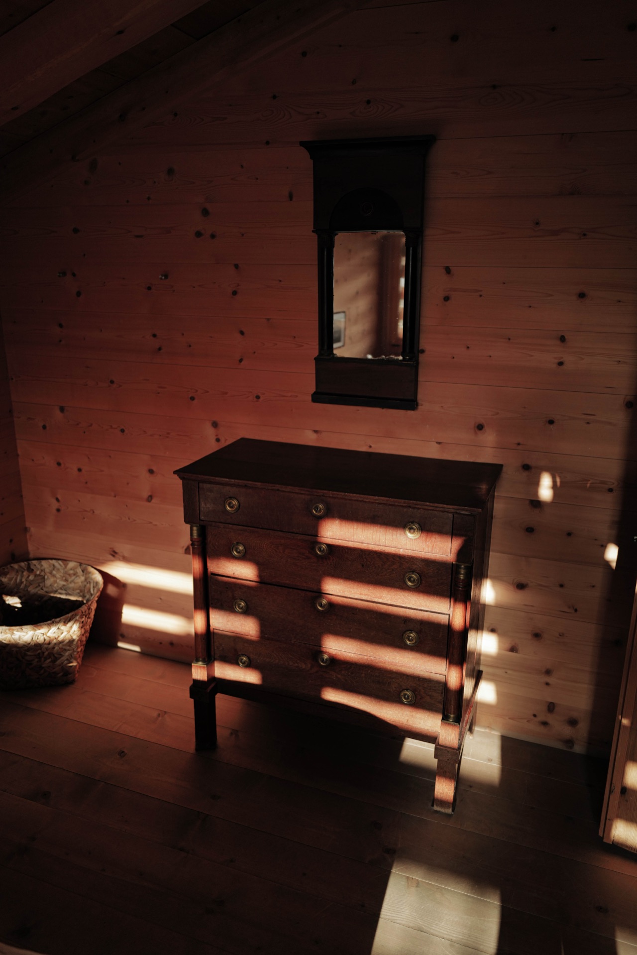 Antique chest of drawers with mirror, warm light playing across timber walls